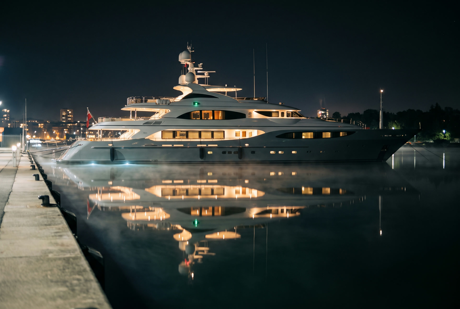 A yacht docked side-on at night, her lights mirrored on calm water